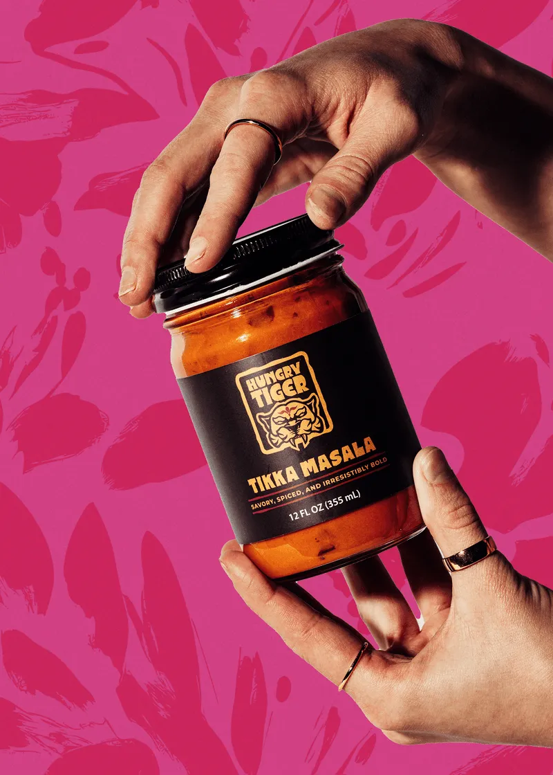 Hands opening a jar of Hungry Tiger Tikka Masala